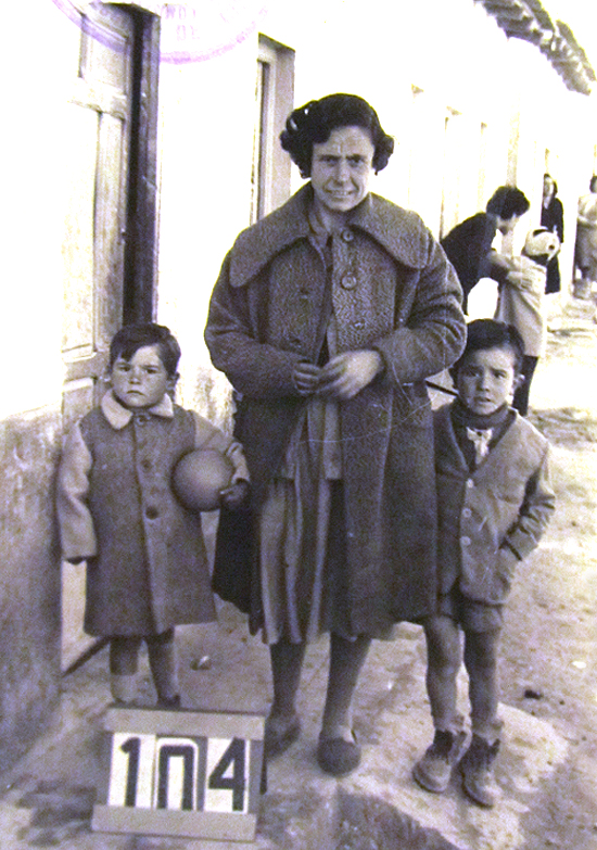 Las fotos son todo un documento de las condiciones de vida de los vecinos. Una madre con sus dos hijos en la puerta de su chabola en el Pozo del Huevo; el de la izquierda lleva un balón bajo el brazo. Al fondo, unas vecinas observan con curiosidad la escena asomadas a las puertas de sus casas. (© Foto: JJMANCHA / Vallecasweb.com) Las fotos son todo un documento de las condiciones de vida de los vecinos. Una madre con sus dos hijos en la puerta de su chabola en el Pozo del Huevo; el de la izquierda lleva un balón bajo el brazo. Al fondo, unas vecinas observan con curiosidad la escena asomadas a las puertas de sus casas. (© Foto: JJMANCHA / Vallecasweb.com)
